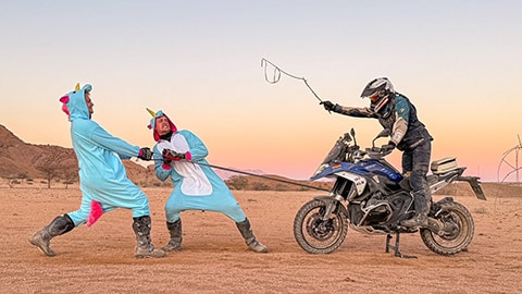 Dos pilotos del equipo masculino alemán, disfrazados de unicornios, tiran de una cuerda de remolque fijada a una R 1300 GS. El tercer piloto está sentado en la moto y blande un látigo.