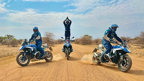El equipo masculino de la India realiza un recorrido en formación con el piloto central más derecho que una vela sobre su moto mientras cruza las manos sobre la cabeza.