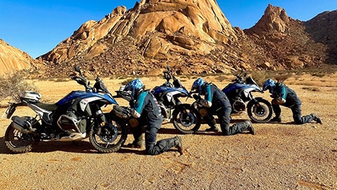 Los tres conductores del equipo masculino indio se arrodillan delante de sus motos.