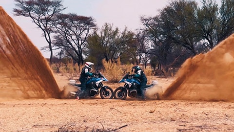 Dos pilotos del equipo internacional se enfrentan con sus ruedas delanteras mientras levantan una impresionante cantidad de arena con las ruedas traseras.