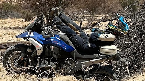 Una conductora del equipo femenino japonés tumbada sobre su R 1300 GS. Las piernas apuntan hacia el manillar, mientras que los hombros y la cabeza se dirigen hacia la parte trasera de la moto.